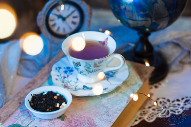 Hot tea in a floral teacup next to a vintage desk clock, a globe, and warm string lights