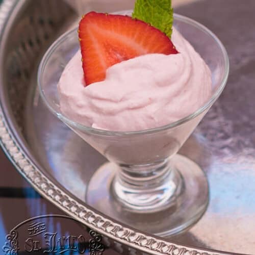 A glass dessert cup filled with pink mousse, topped with a sliced strawberry and a mint leaf, sits on a silver tray with an engraved “St. James Tearoom” logo.