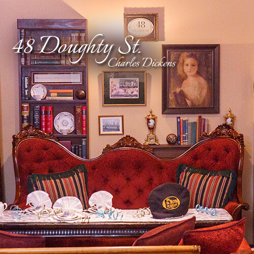 48-Doughty-St-Charles-Dickens-Seating-Area-Teatime-Parlor-The-St-James-Tearoom Ornate red velvet sofa behind a fully set afternoon tea table with decorative ribbons