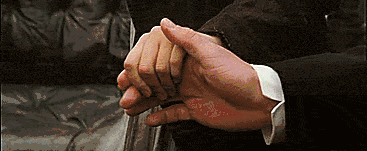 A person gently holds and rubs another person’s hand for comfort while sitting on a dark leather couch.