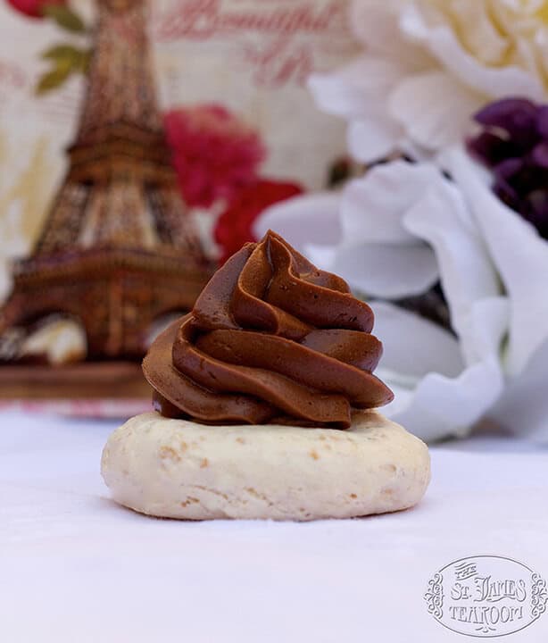 A cookie topped with a swirl of chocolate cream sits in front of blurred flowers and an Eiffel Tower image, creating a Parisian ambiance.