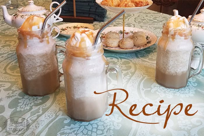 Three glass mugs of Butterbeer Ice Cream Floats, topped with ice cream and caramel sauce, sit on a patterned tablecloth, with a teapot, plates, and scones in the background. The word “Recipe” is written on the image.