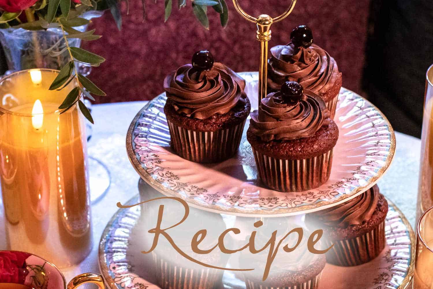 Chocolate cupcakes with swirled frosting and cherries on top, arranged on a two-tiered plate stand, are surrounded by candles and flowers, creating a charming setting perfect for any occasion. The word “Recipe” is written across the image, inviting you to enjoy these treats alongside your favorite iced tea recipe for a delightful pairing.