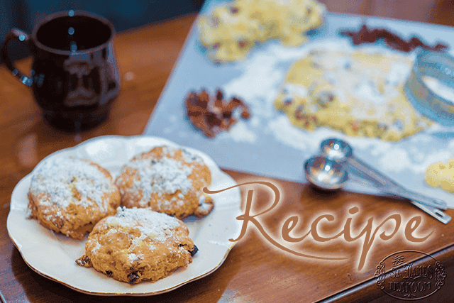 Three powdered sugar cookies on a plate, mixing spoons, dough, and a mug on a table evoke cozy holiday baking moments. “Recipe” is written in script over the image—a scene reminiscent of preparing Christmas Stollen Scones.