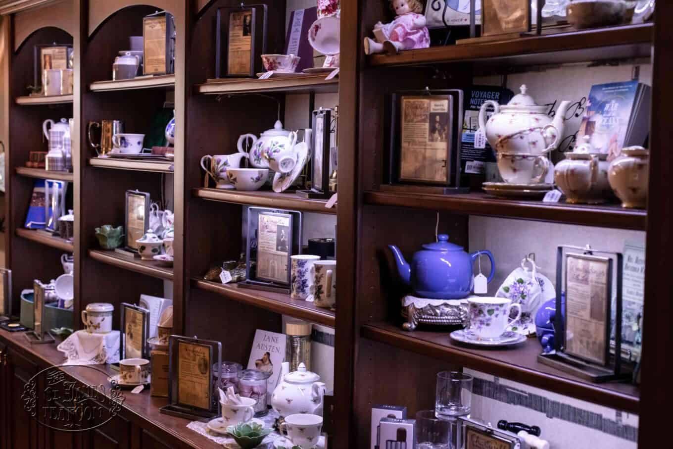 Wooden shelves display vintage teapots, teacups, framed photos, books, and porcelain dolls, all arranged neatly in a cozy, antique-style setting. The collection evokes a nostalgic and elegant atmosphere.