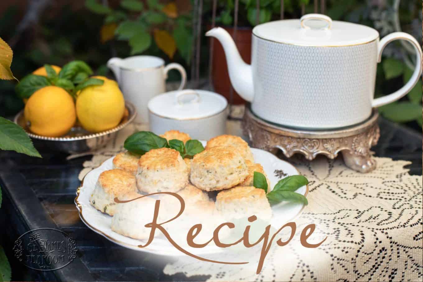 A plate of Basil Lemon Scones with green garnish sits on a lace tablecloth next to a teapot, sugar bowl, cup, and a bowl of lemons. The word “Recipe” is overlaid on the image.