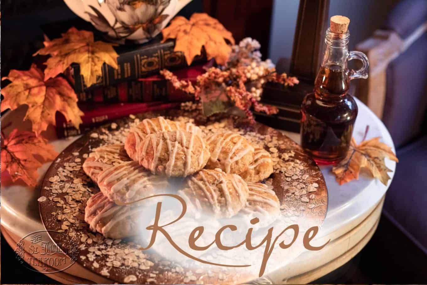 A plate of glazed pastries sits on a table with oats scattered around, surrounded by autumn leaves, books, berries, and a bottle of syrup—capturing the cozy essence of an easy maple oat scone recipe. The word “Recipe” is written in large script across the image.