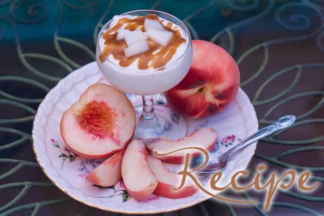 A glass of yogurt topped with caramel and fruit sits on a plate with sliced peach, a whole peach, and a spoon. The word “Recipe” is overlaid on the image.