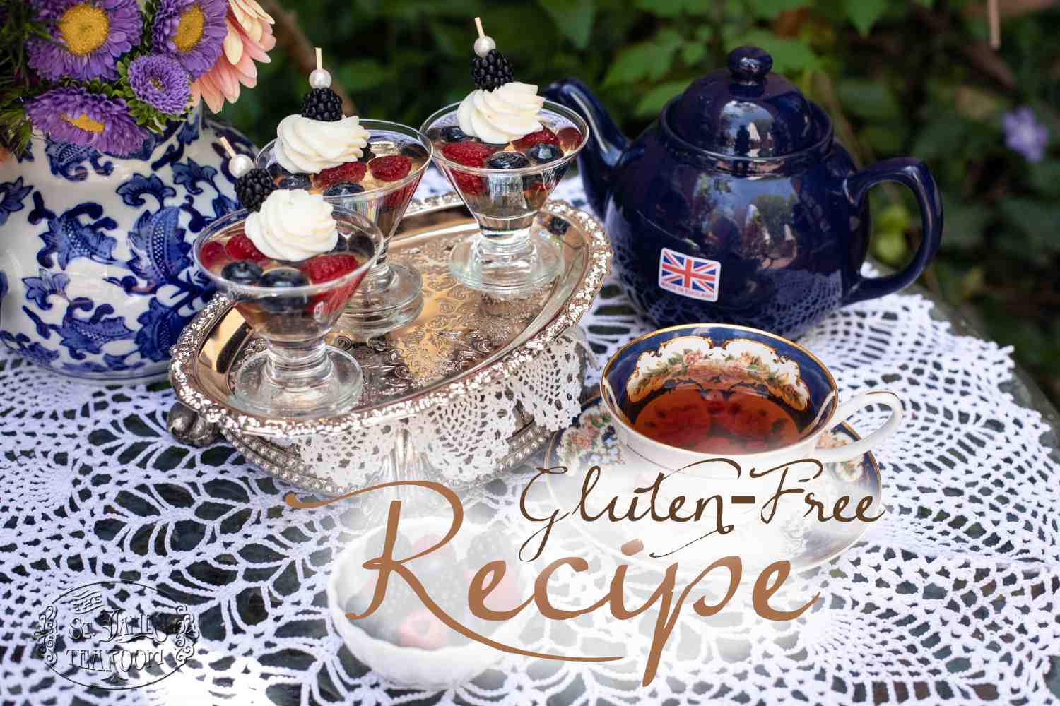 Three parfaits with berries and cream on a silver tray, blue teapot with UK flag, teacup with tea, and flowers on a lace tablecloth. Text reads “Gluten-Free Recipe.” Inspired by The St. James Tearoom’s Sparkling Wine Berry Gelatin Recipe.