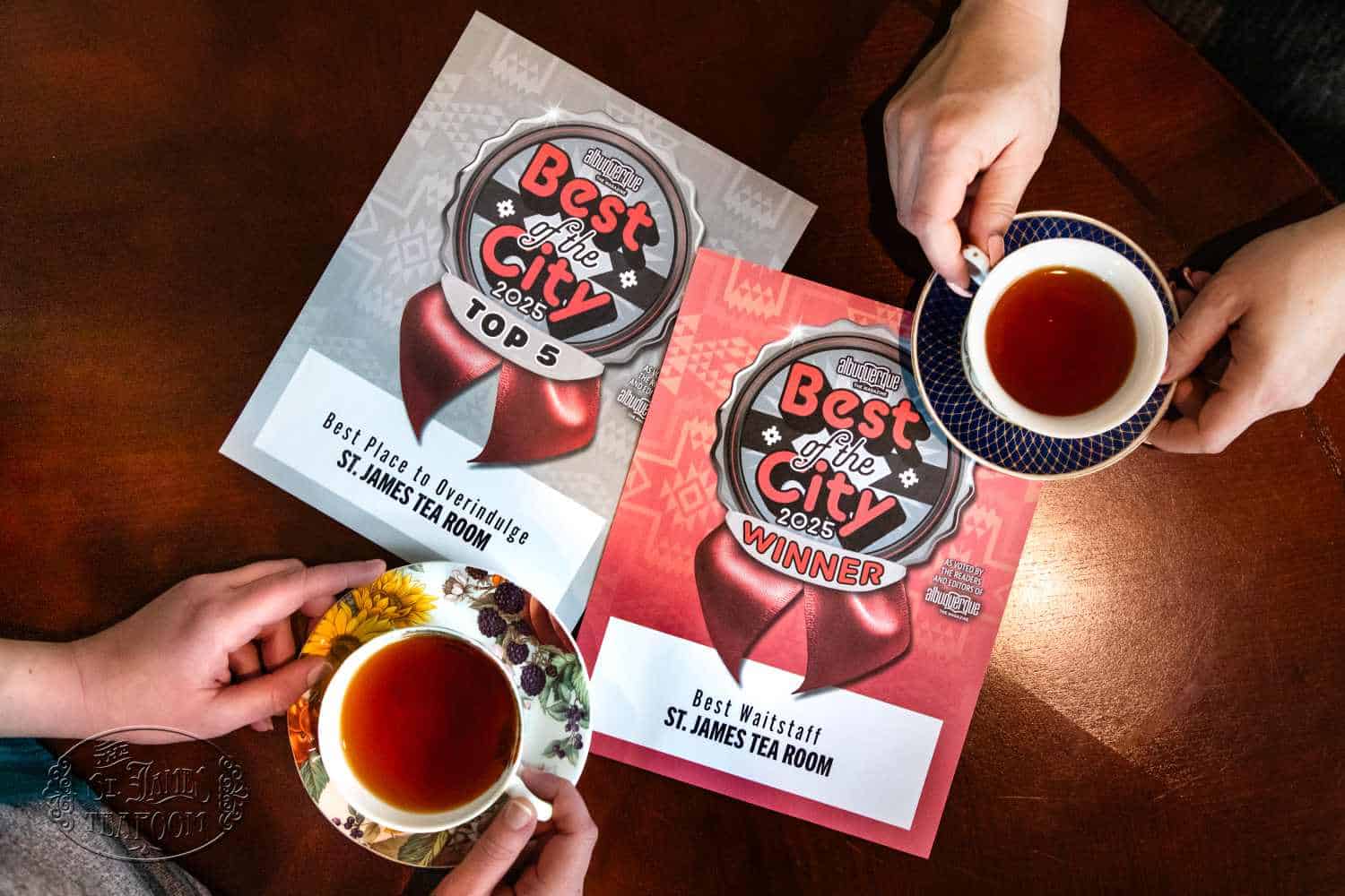 Two people hold teacups over a table with two award certificates for St. James Tearoom, recognizing them as “Best of the City 2023” winner and “Top 5” in different categories—even earning a place among Yelp’s Top 100 Restaurants this year.