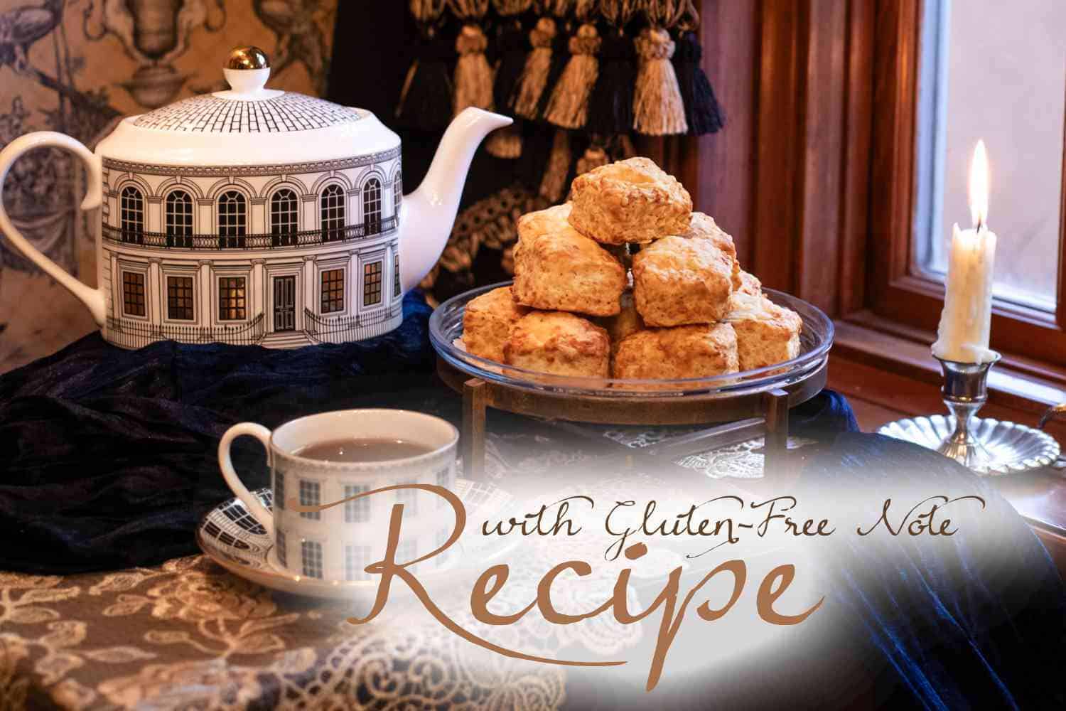 A teapot, teacup, and plate of scones—made using our White Cheddar Black Pepper Scones Recipe—sit on a table by a window, with a lit candle and text overlay reading “Recipe with Gluten-Free Note.” Elegant, cozy tea setting.