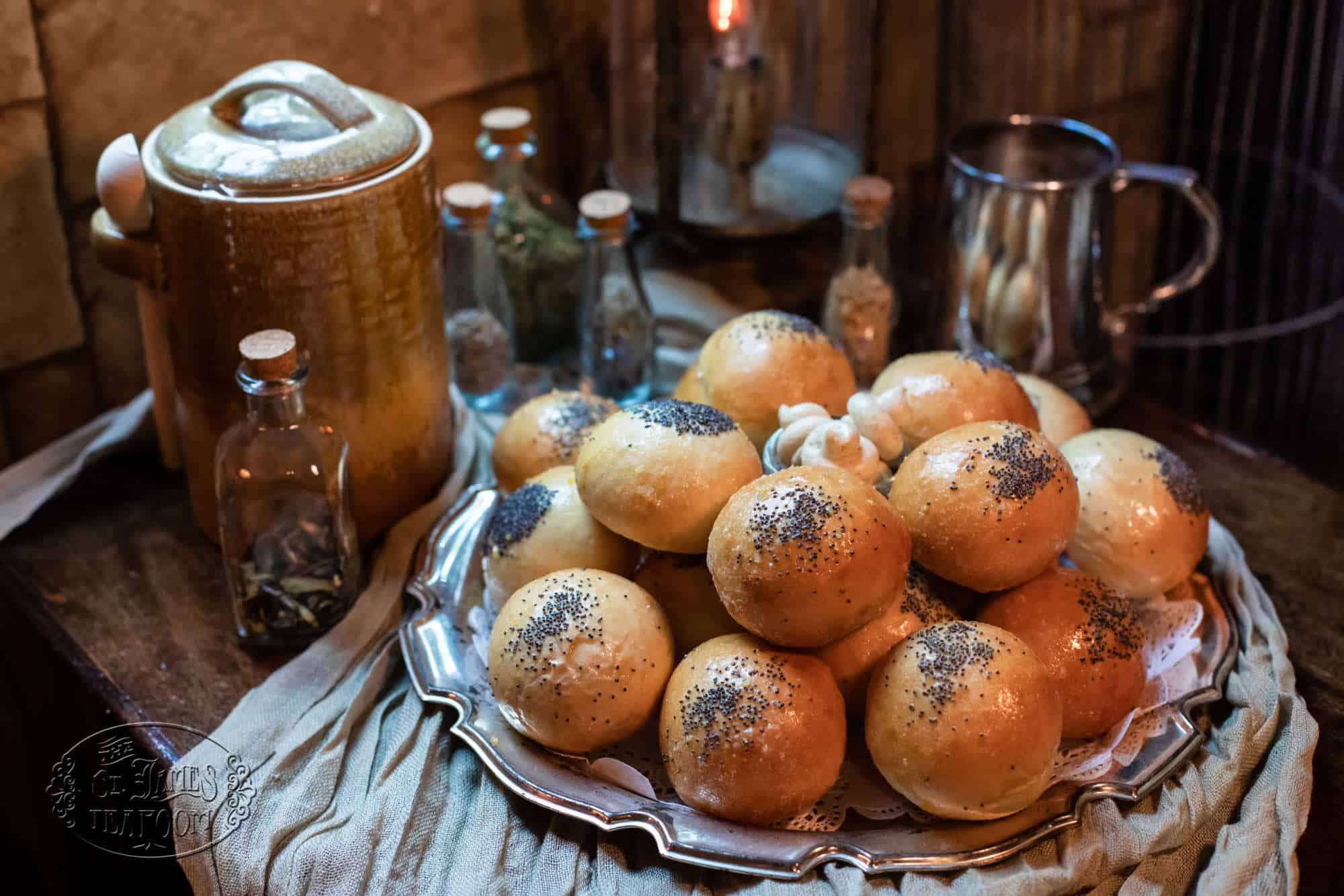 A silver platter piled high with golden-brown bread rolls topped with poppy seeds.